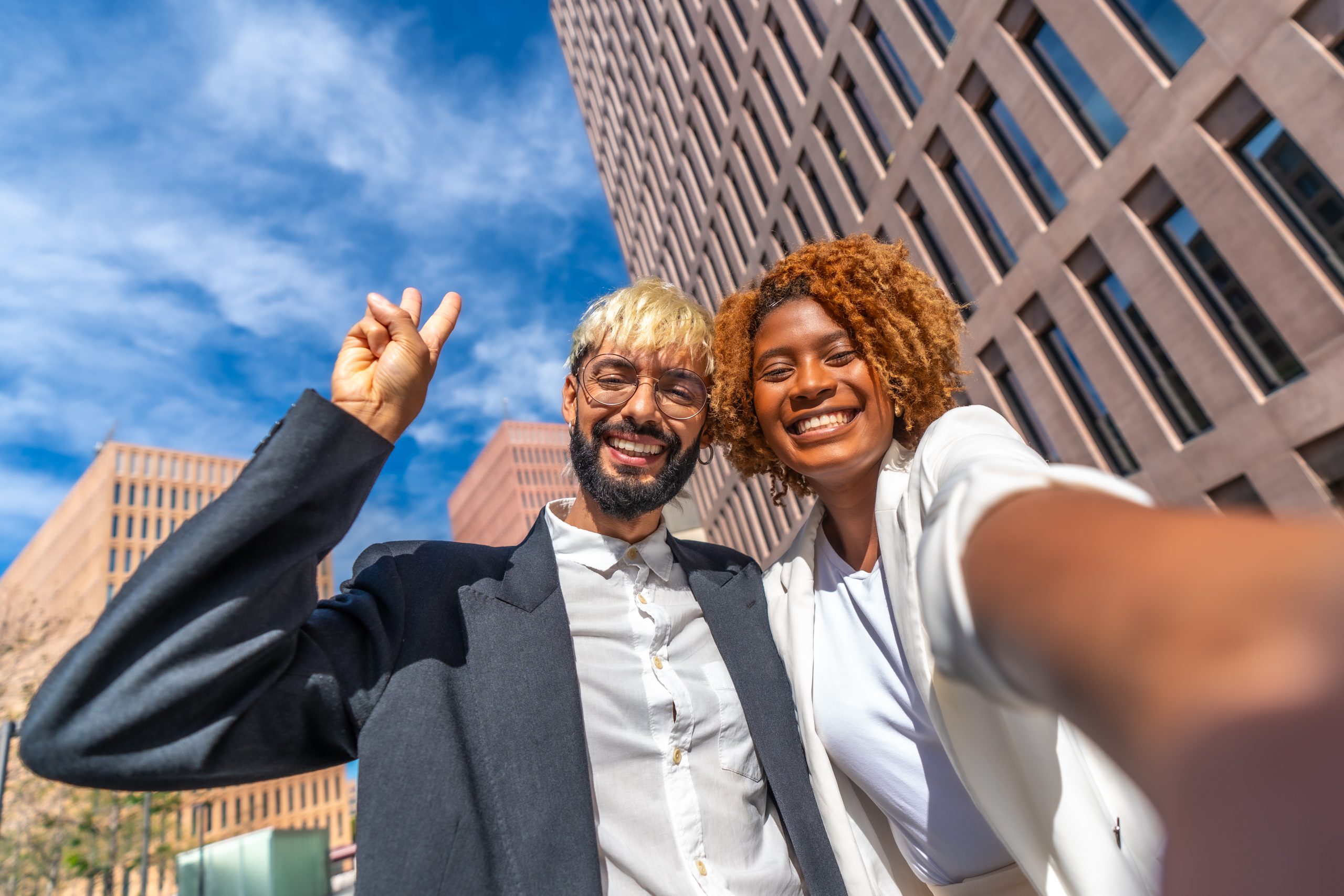 Frontal close-up portrait of two young multi-ethnic lawyers or business people taking a selfie outdoors for social media marketing.